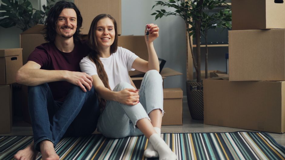 A smiling homeowner holds up a set of house keys in a bright, modern living room, illustrating the financial success of saving money on commissions.